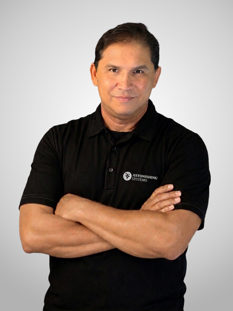 Man with arms crossed wearing a black polo shirt featuring an Astonishing Systems logo, against a light gray background.