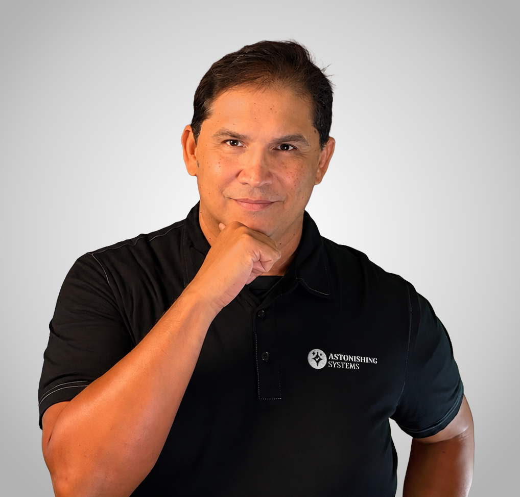 Portrait of a man in a black polo with the Astonishing Systems logo, hand resting on his chin against a gray gradient background.