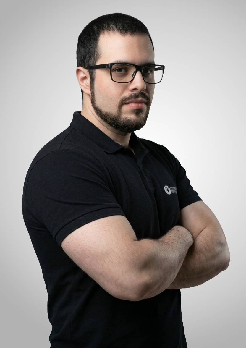Man with dark hair and beard in a black polo and glasses, arms crossed against a gray gradient background.