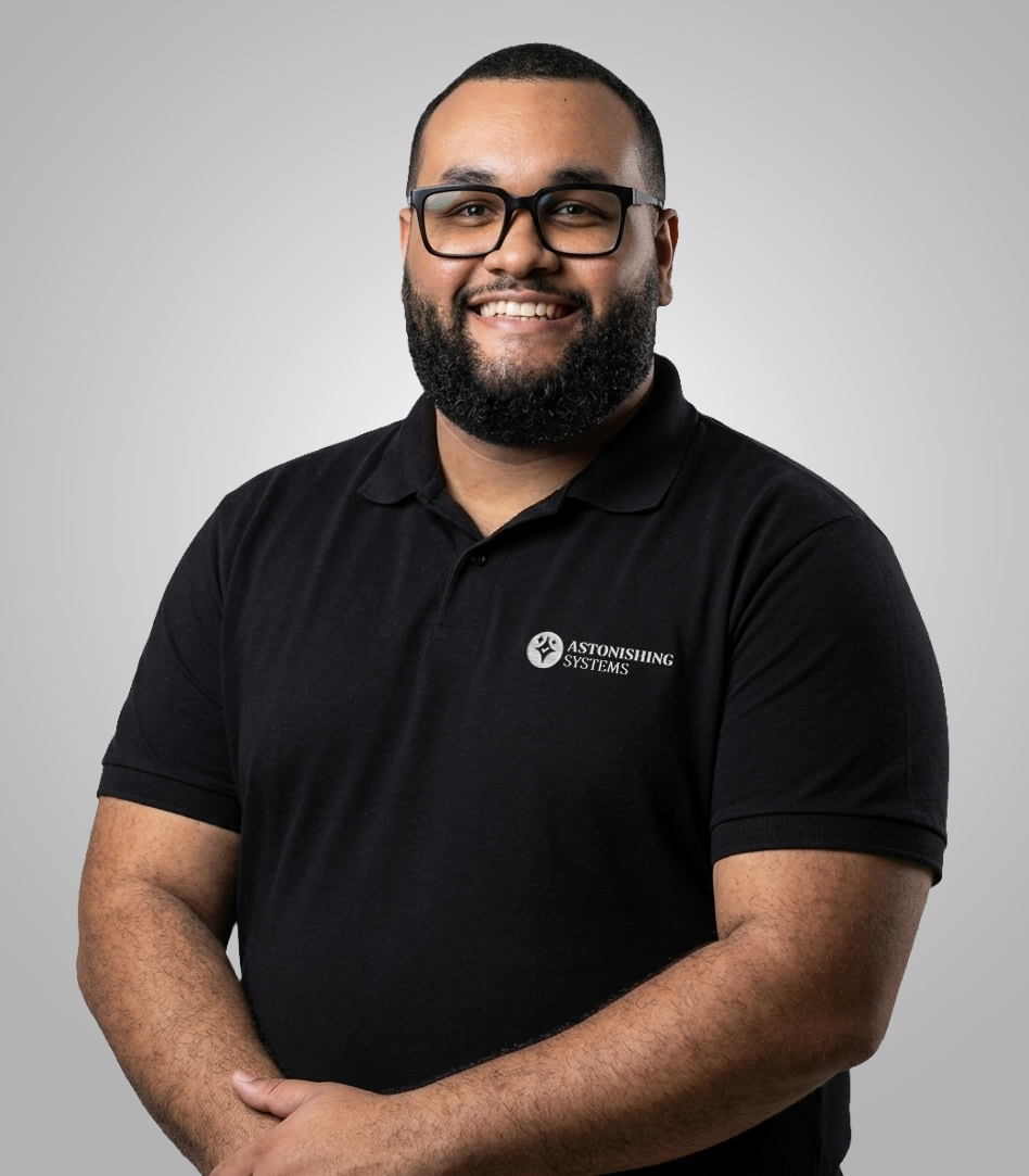 Smiling man with glasses wearing a black polo shirt featuring the Astonishing Systems logo on the chest area.